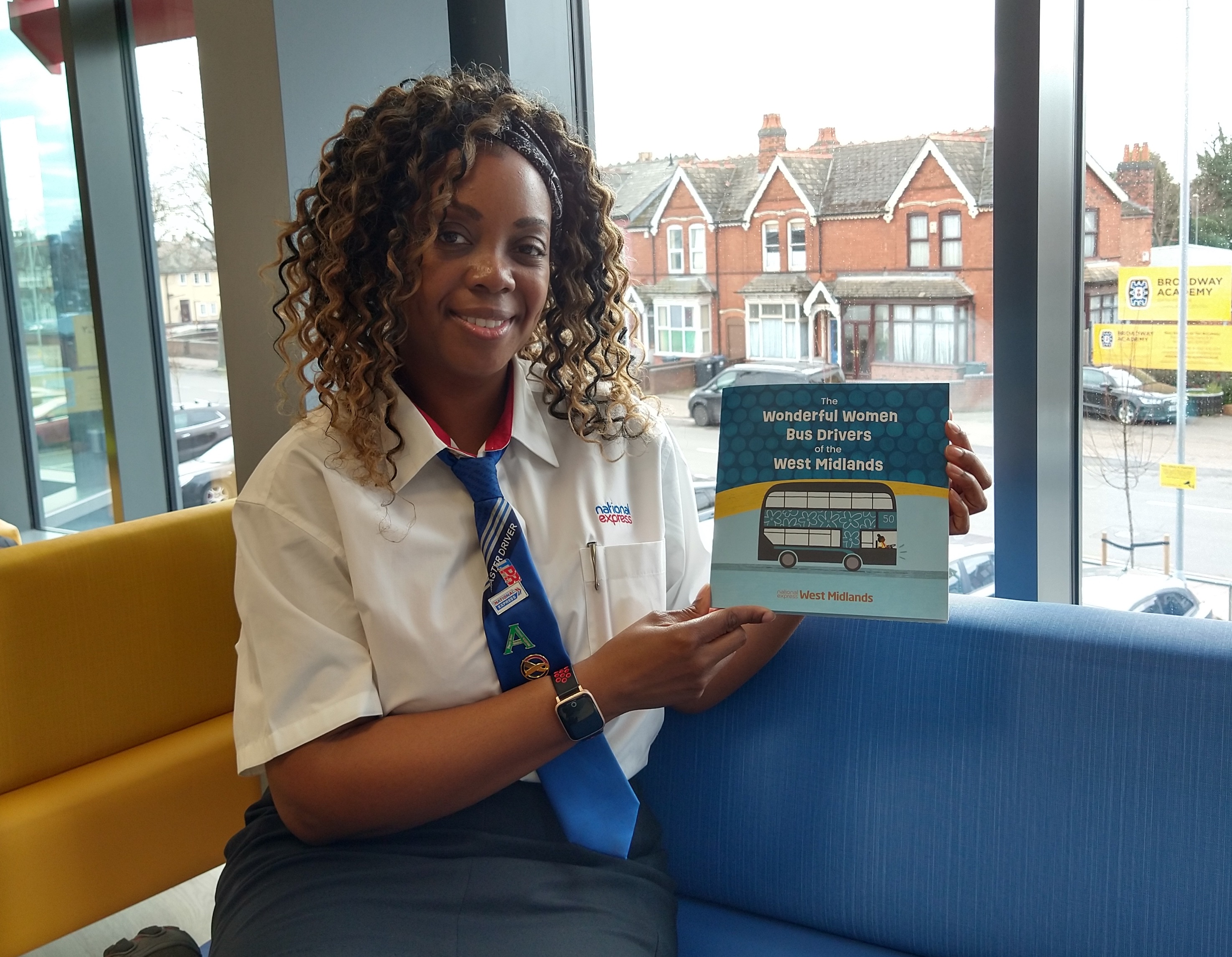Black female Bus Driver, Diane Reid holding up a National Express produced children's book about female bus drivers, of which she is featured in.
