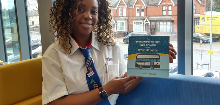 Black female Bus Driver, Diane Reid holding up a National Express produced children's book about female bus drivers, of which she is featured in.